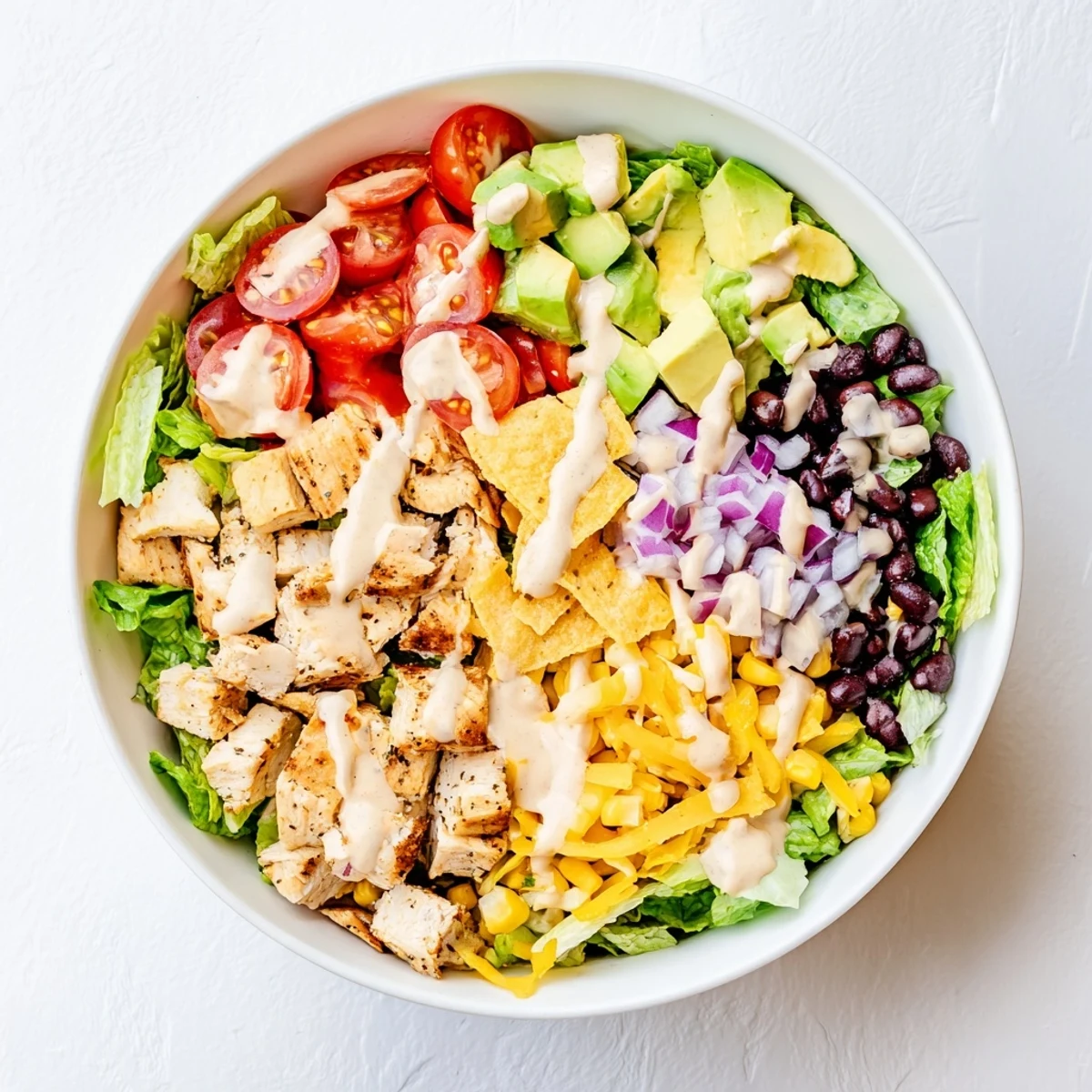 Farbenfrohe Chicken Taco Chopped Salad mit knackigem Salat, gewürztem Hähnchen und zerbröselten Tortilla-Chips auf weißem Teller.