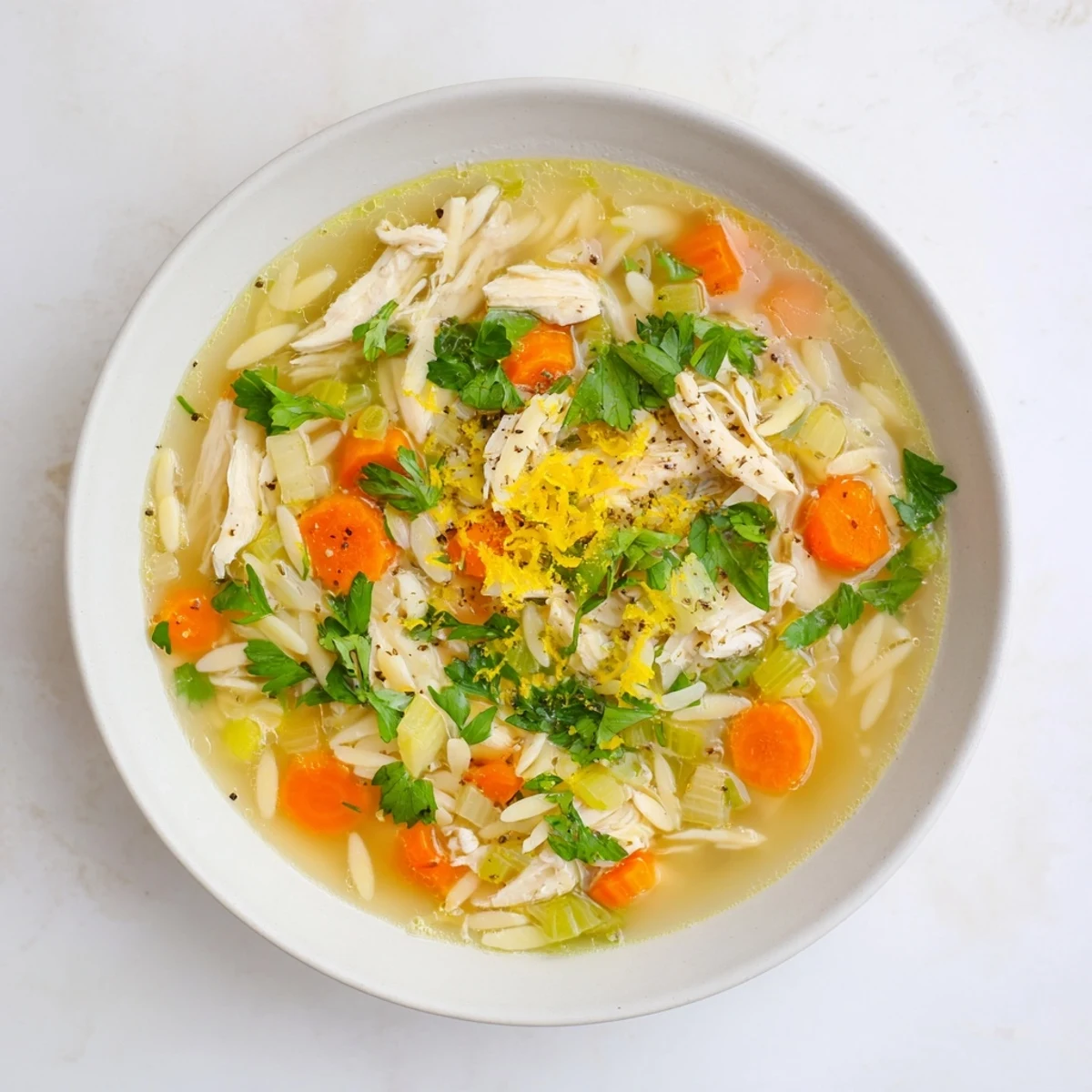 Frisch gekochte Lemon Pepper Chicken Orzo Soup in einer Hellblau-glasurten Keramikschüssel, dampfend serviert mit zitroniger Note und schwarzem Pfeffer.