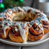 Festlicher King Cake-Zimtschnecken-Kranz mit goldener Glasur und bunten Streuseln, serviert auf einer festlichen Platte.