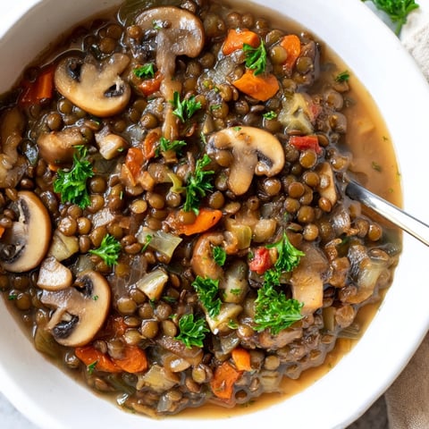 Herzhafter Linsen-Pilz-Eintopf dampft, mit Kräutern bestreut, in einer rustikalen Schüssel serviert.