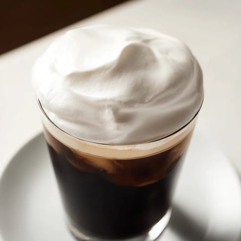 Fluffy Starbucks cold foam, swirled atop a chilled iced coffee, promising a creamy, sweet treat.