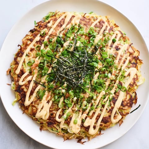 Savory Japanese okonomiyaki pancakes, bubbling on a skillet, topped with rich okonomiyaki sauce and bonito flakes.