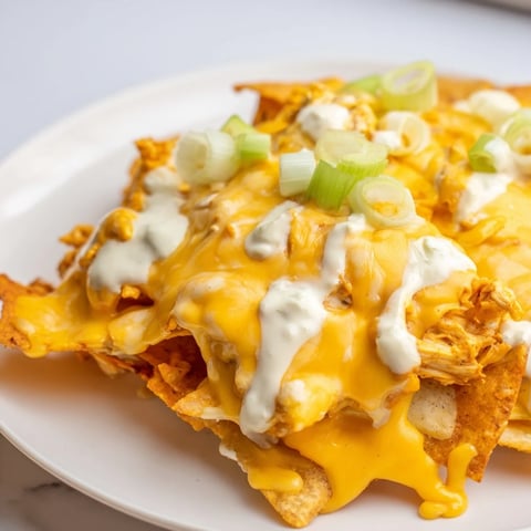 Crispy baked Buffalo Chicken Nachos loaded with melted cheddar, Monterey Jack, and a cool ranch drizzle, served hot.