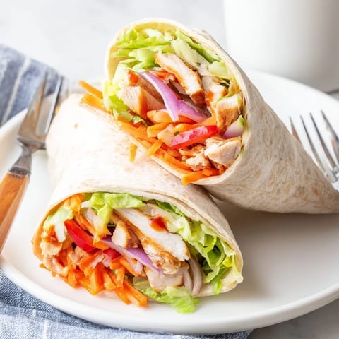 A close-up view of a Honey Sriracha Chicken Wrap halved to reveal saucy, tender chicken and colorful veggies.