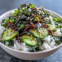Reisbowl mit Seetang und Nori: bunter Teller mit Sushi-Reis, knackiger Gurke und gerösteten Sesamkörnern.